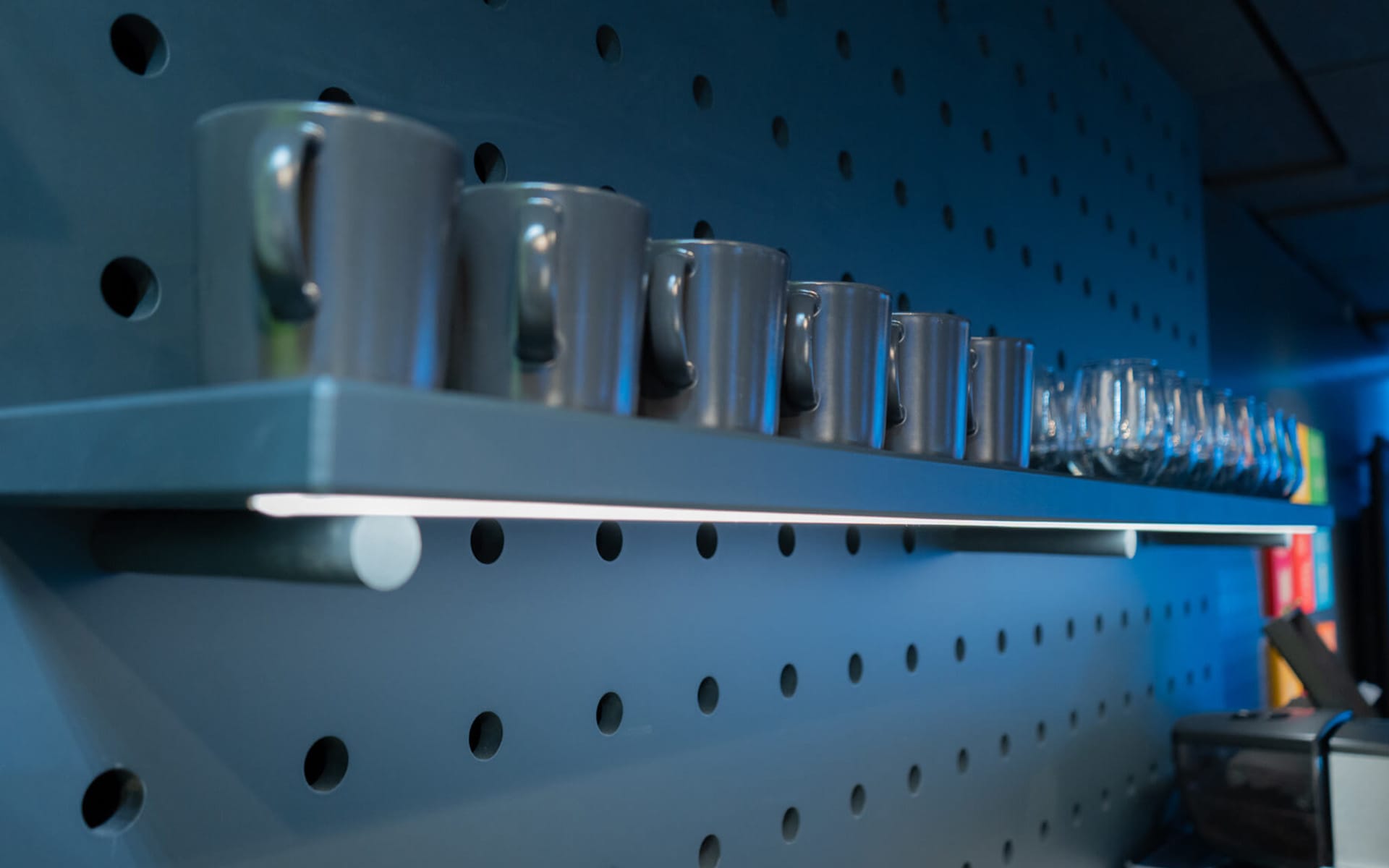 Colour-matched cups on kitchen shelf with integrated LED lighting, Atlas Copco showroom