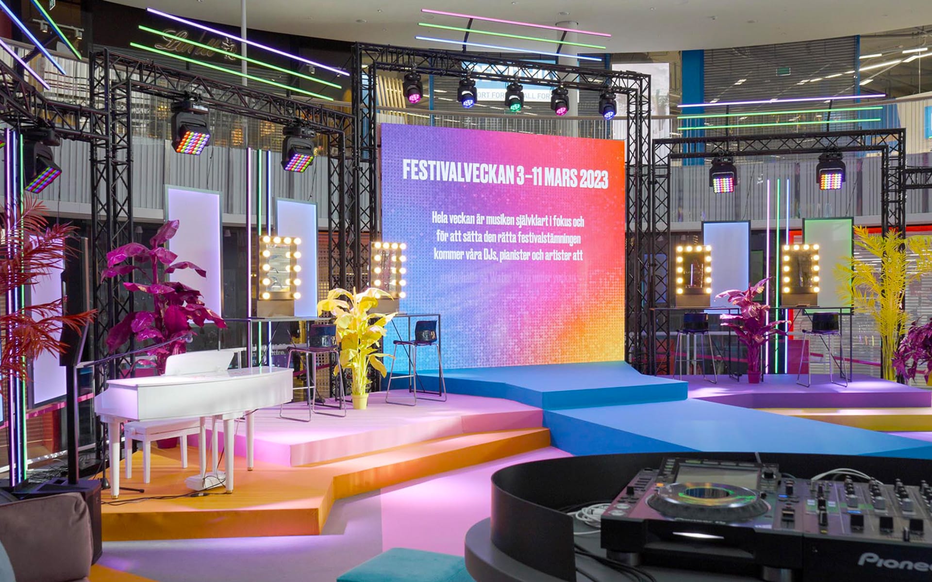 Multi-coloured stage design with platforms and catwalk seen from DJ booth, Festival Week MOS 2023