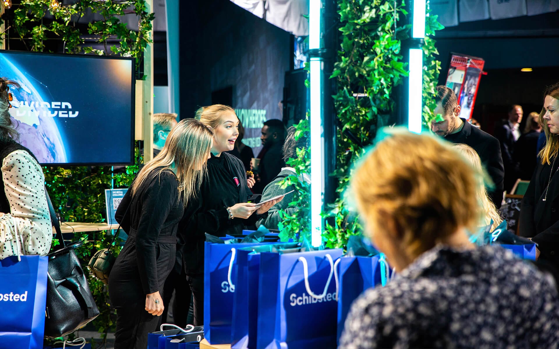 Hosts handing out giveaways from seating unit storage in Schibsted's stand, NextM Annexet